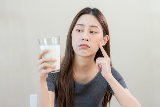 Allergy asian young woman, girl looking, holding glass of milk, face in thinking before drink milk as it may upset her stomach ache, pain. Lactose intolerance and dairy food , health problem concept. photo