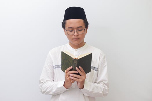 Portrait of young Asian muslim man reading and reciting Holy book of Quran seriously. Isolated image on white background photo