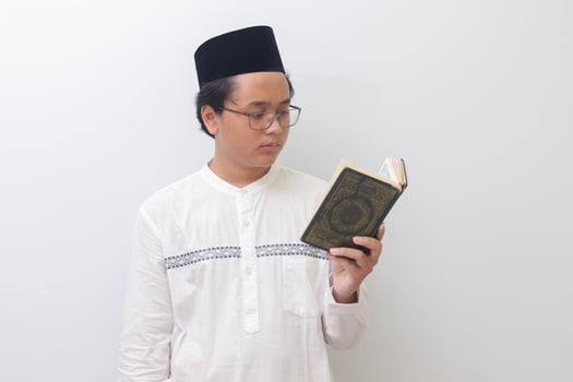 Portrait of young Asian muslim man reading and reciting Holy book of Quran seriously. Isolated image on white background photo
