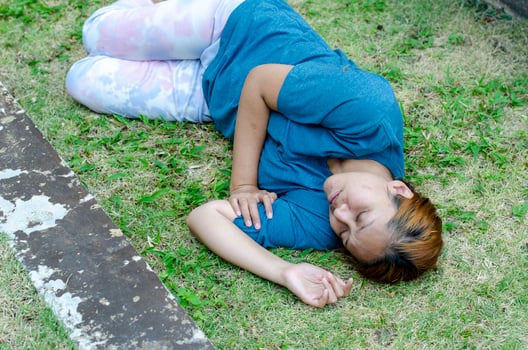Asian woman lying on her side fainting on grass in the park in summer because of the hot weather photo