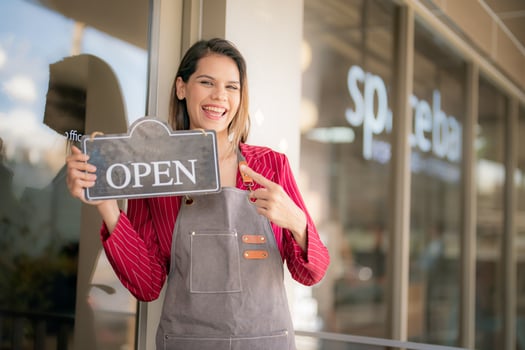 A woman holding an open sign in front of a business photo