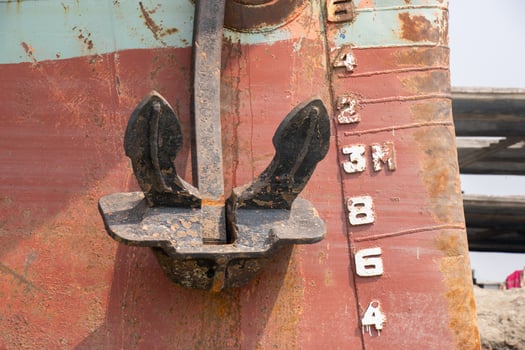 Rusty ship anchor and metal surface close-up view. Rusty ship body close-up with water level meter. Old and abandoned ship with anchor closeup. Heavy ship body parts on a riverbank. photo