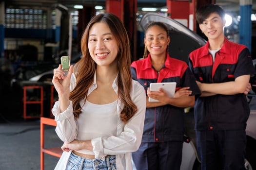 Young Asian female customer shows car key with automotive mechanic workers, happy smile in quality trust at maintenance garage, professional vehicle service center, fix check and repair auto industry. photo