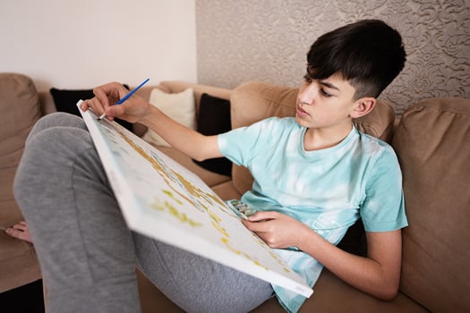 Young male teenager painting picture by numbers on canvas in living room at home. Hobby and leisure concept. photo