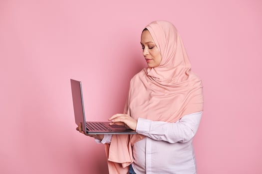 Multitasking Arab Muslim pregnant woman in pink hijab, typing text on laptop keyboard. Pregnancy, business and career photo