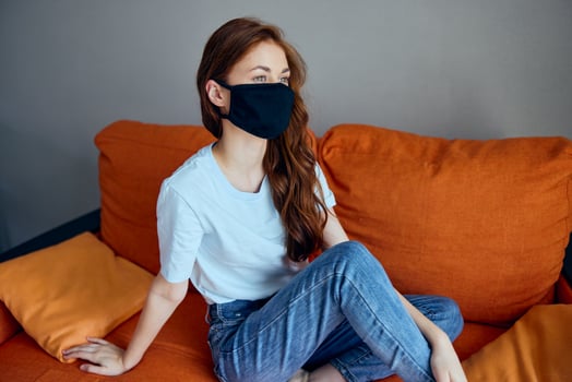 portrait of a woman wearing a mask sits on an orange sofa at home Lifestyle photo
