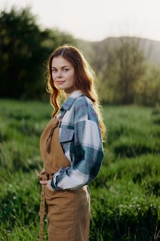 A woman gardener in an apron stands in a field of green grass outdoors, smiling on a summer day into a sunset photo