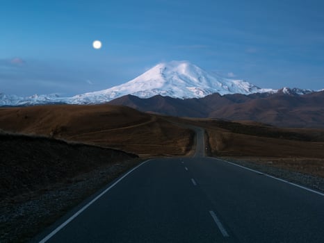 Morning landscape with winding highway to Mount Elbrus under morning sky with full moon. Empty road disappear into the distance at twilight. Way with markup perspective view. Kabardino-Balkaria. photo