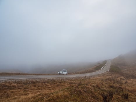 Morning mountain highway in dense fog. White car SUV with fog li photo
