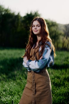 A farmer woman in her work clothes, plaid shirt and apron, stands in the field on the green grass and smiles in the setting sun photo