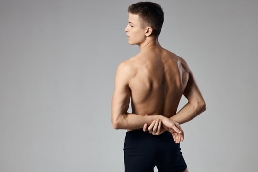 a man with pumped up muscles holds his hands behind his back on a gray background and behind photo