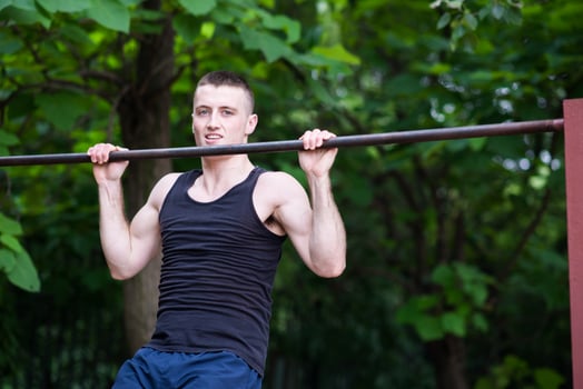 strong man doing pull-ups on a bar outdoor photo