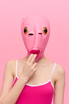 Funny woman in a sexy costume with a pink fish mask on her head put her fingers in her mouth in pink clothes on a pink background. The concept of modern art photography photo