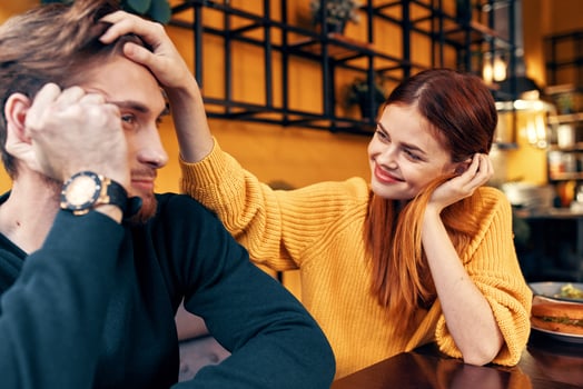 happy woman in a sweater gestures with her hands fun emotions and a man in a sweater sits in a cafe photo