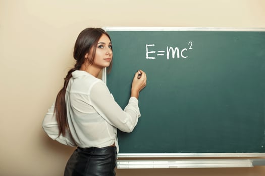 Beautiful young girl teacher writing formula on the blackboard. photo