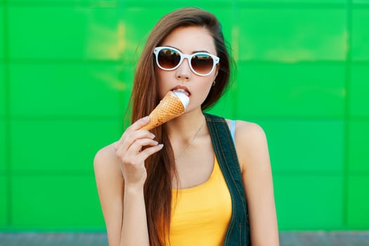 Beautiful young girl eating ice cream near the green wall.Stylish beautiful girl with ice-cream stands near green metal wall. photo