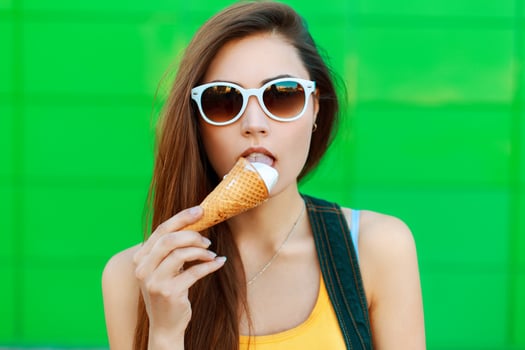 Young beautiful woman in sunglasses eating ice cream on a green background. photo