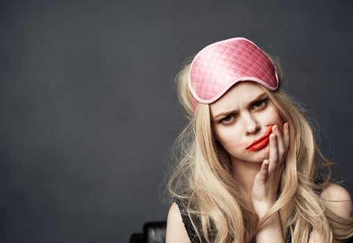 A blonde with bright makeup on her face and a pink sleep mask on her head photo