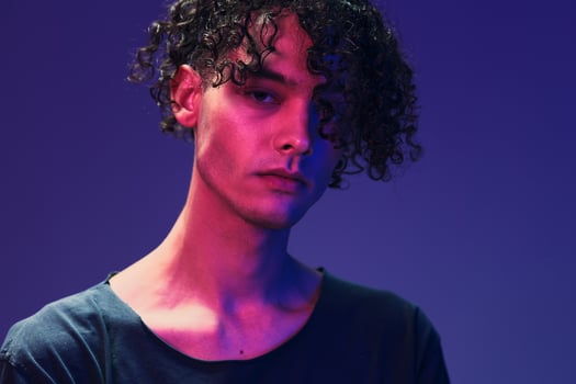 Stylish tanned curly man in black t-shirt looks at camera posing isolated on color pink blue studio background. Cool fashion offer. Virtual Reality New Collection concept. Copy space for ad photo