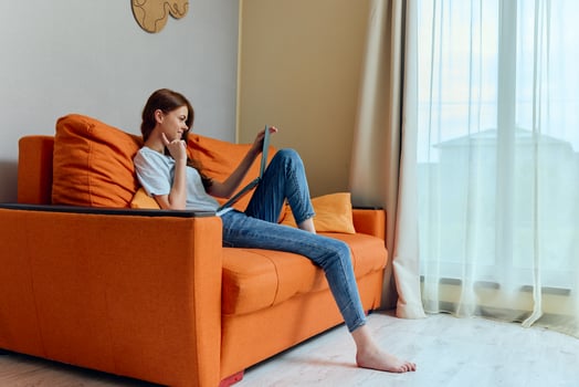 smiling woman chatting on the orange couch with a laptop unaltered photo