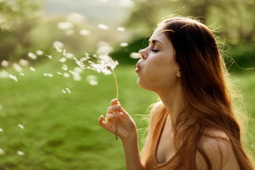 Woman with a dandelion flower in her hands smiling and blowing on it against a background of summer greenery and sunlight photo