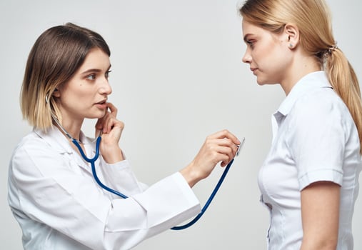doctor with a stethoscope examines a woman in a white t-shirt on a light background photo