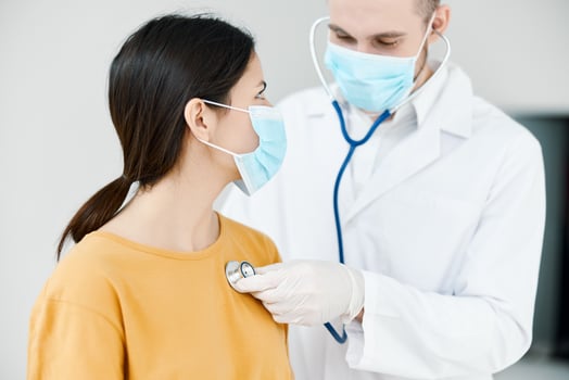 doctor with stethoscope listens to heartbeat of patient wearing medical mask in hospital photo
