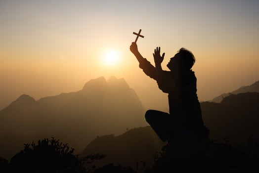 Silhouette of faithful man praying with Christian cross at sunset as concept for religion, faith, prayer and spirituality. photo
