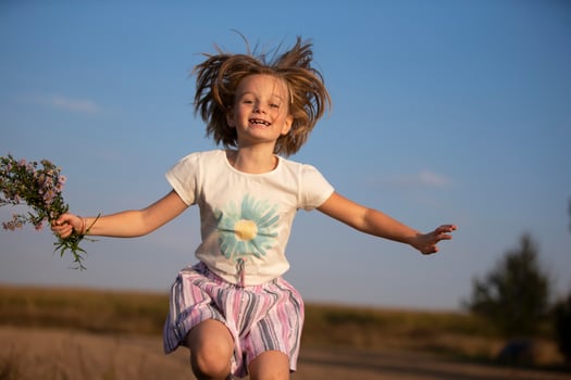 A beautiful joyful little girl in a meadow with a bouquet of flowers is jumping. A child in a beautiful summer field. photo