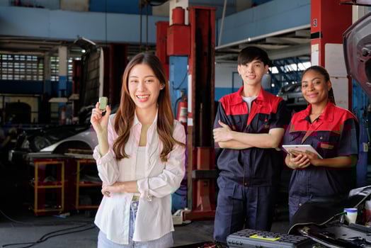 Young Asian female customer shows car key with automotive mechanic workers, happy smile in quality trust at maintenance garage, professional vehicle service center, fix check and repair auto industry. photo