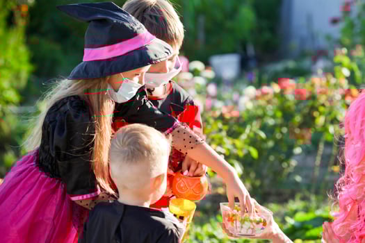 Children trick or treat in Halloween costume and medical mask. A little boy and a girl in suits during the coronavirus pandemic receive candy from a woman dressed as a witch. photo
