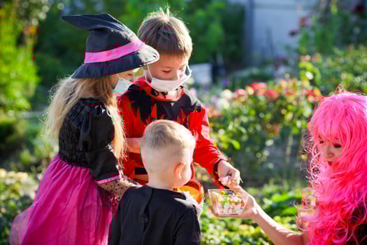 Children trick or treat in Halloween costume and medical mask. A little boy and a girl in suits during the coronavirus pandemic receive candy from a woman dressed as a witch. photo