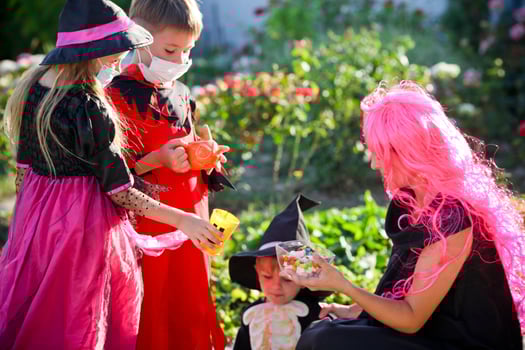Children trick or treat in Halloween costume and medical mask. A little boy and a girl in suits during the coronavirus pandemic receive candy from a woman dressed as a witch. photo