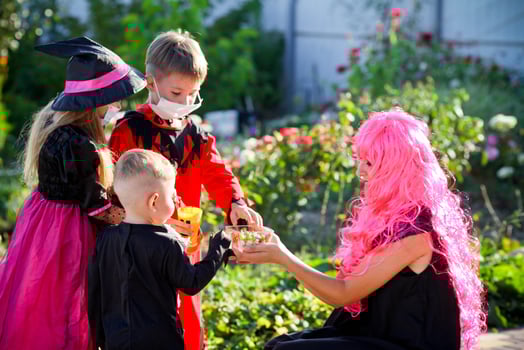 Children trick or treat in Halloween costume and medical mask. A little boy and a girl in suits during the coronavirus pandemic receive candy from a woman dressed as a witch. photo