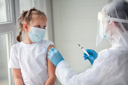 Doctor is hands in rubber gloves makes a shot in the shoulder of a child in a medical mask. Vaccination against coronavirus. COVID-19 vaccine. The doctor vaccinates the child  gets a flu shot. photo