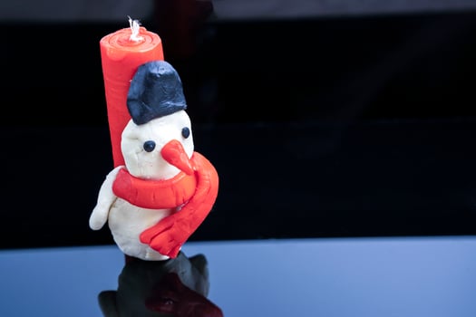 homemade children's candle in the form of a snowman on a glossy black glass background photo