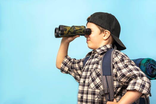 boy tourist looks through binoculars on a blue background, copy space photo