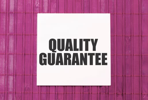 blank note pad with text quality guarantee on blue wooden background photo