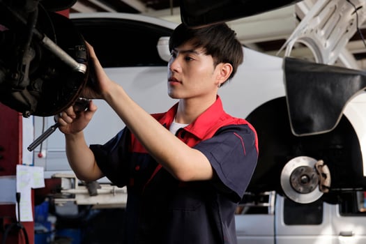 One young expert Asian male automotive mechanic technician is screwing car wheel nuts on lifting with wrench for repair at garage. Vehicle maintenance service works, industry occupation business jobs. photo