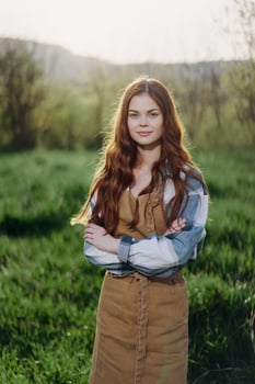 A farmer woman in her work clothes, plaid shirt and apron, stands in the field on the green grass and smiles in the setting sun photo
