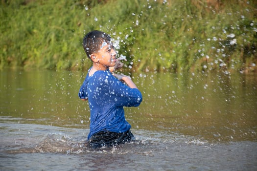 Asian boy in blue t-shirt is spending his freetimes by diving, swimming, throwing rocks and catching fish in the river happily, hobby and happiness of children concept, in motion. photo