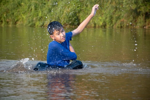 Asian boy in blue t-shirt is spending his freetimes by diving, swimming, throwing rocks and catching fish in the river happily, hobby and happiness of children concept, in motion. photo