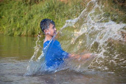 Asian boy in blue t-shirt is spending his freetimes by diving, swimming, throwing rocks and catching fish in the river happily, hobby and happiness of children concept, in motion. photo