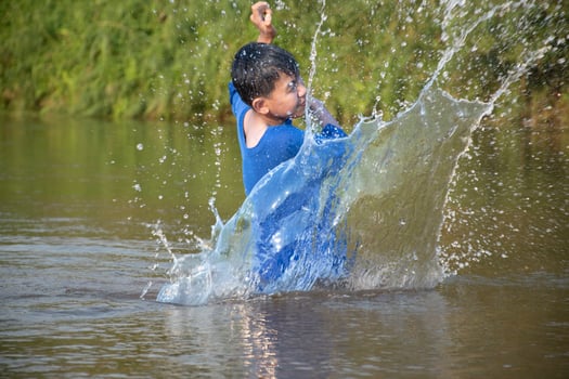 Asian boy in blue t-shirt is spending his freetimes by diving, swimming, throwing rocks and catching fish in the river happily, hobby and happiness of children concept, in motion. photo
