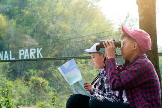 Asian boys holding binoculars and national map and reading map details about bird watching and fish watching by the river bank in local national park, nature study and environment learning concept. photo