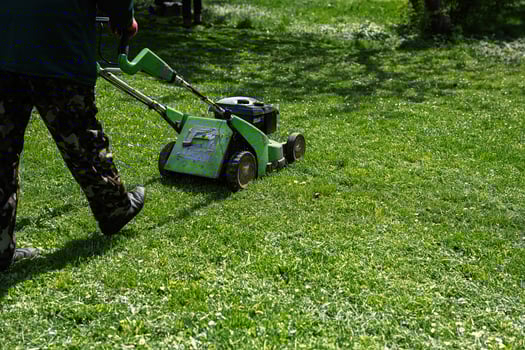 Communal services gardener worker man using lawn mower for grass cutting in city park. photo