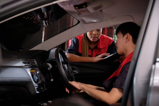 Young male Asian automotive mechanic technician and partner checking maintenance list with tablet in car interior at garage. Vehicle service fix and repair works, industrial occupation business jobs. photo