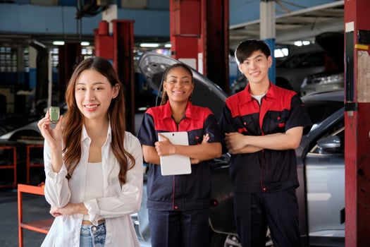 Young Asian female customer shows car key with automotive mechanic workers, happy smile in quality trust at maintenance garage, professional vehicle service center, fix check and repair auto industry. photo