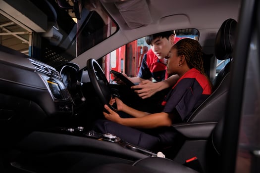 Young Black woman automotive mechanic technician and partner checking maintenance list with tablet in car interior at garage. Vehicle service fix and repair works, industrial occupation business jobs. photo