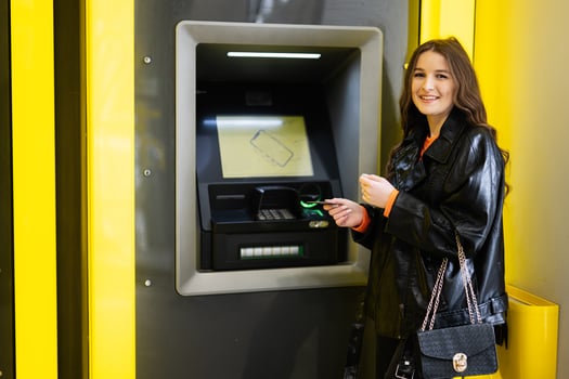 Young brunette girl withdrawing money from credit card at yellow ATM. photo